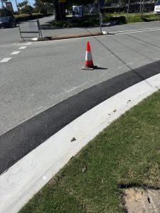 Fresh asphalt patch along kerb; neat join to concrete kerb and lawn (traffic cone in frame). Asphalt Repairs Brisbane